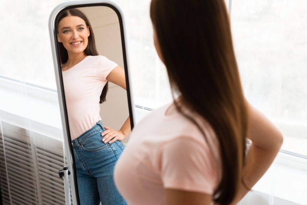 Woman smiling in mirror after several months on semaglutide for medical weight loss